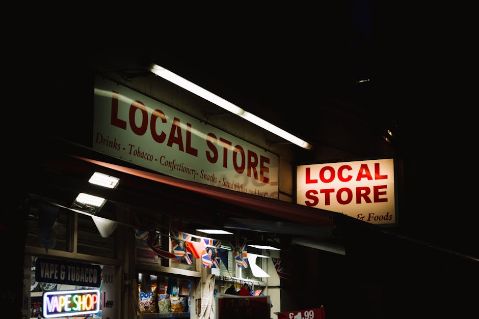 A street-level view of a small retail unit with a prominent green and white sign reading 'GREEN SHOP' above the entrance, situated in front of a pink two-story building with white-framed windows. The 